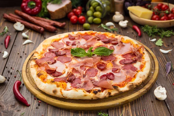 Lezzetli İtalyan pizza jambon, Bavyera sosis ve fesleğen tarafından dekore edilmiş prosciutto ile ahşap arka plan üzerinde bırakır