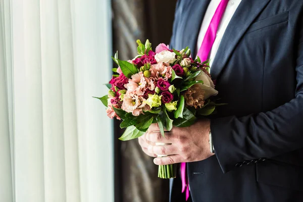 man holding bridal bouquet in hands, groom getting ready in the morning before wedding ceremony