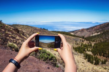 Tenerife, Kanarya Adaları, İspanya üzerinde fotoğrafta telefonunu şaşırtıcı dağlar peyzaj ile genç bir kadın. Seyahat kavramı