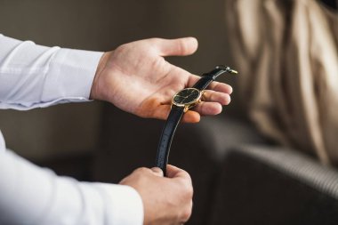 İş adamı kol saatini kontrol ediyor, saati eline alıyor, damat düğün töreninden önce hazırlanıyor.