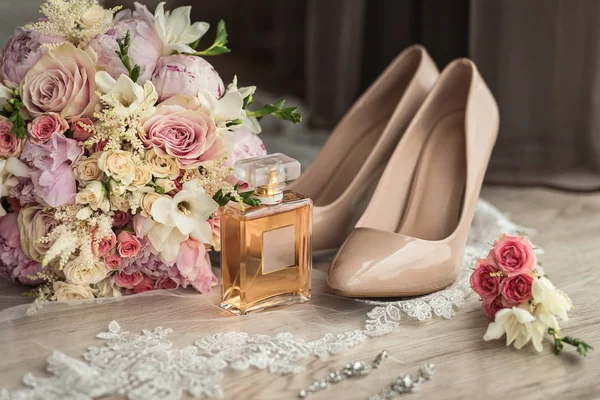 bridal accessories such as shoes, earrings, bouquet and perfume lie on a table