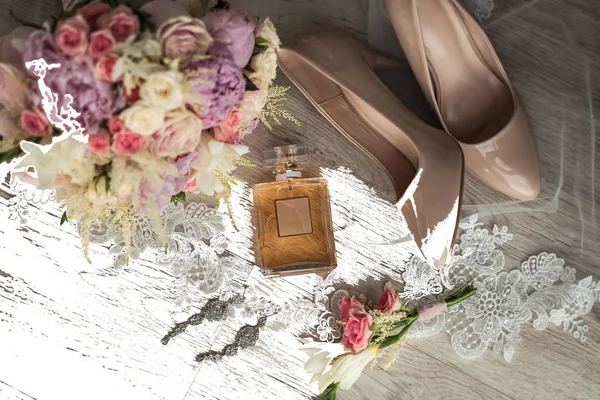 bridal accessories such as shoes, earrings, bouquet and perfume lie on a table