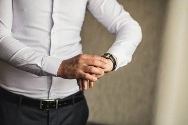 İş adamı kol saatini kontrol ediyor, saati eline alıyor, damat düğün töreninden önce hazırlanıyor.
