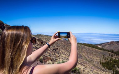 Tenerife, Kanarya Adaları, İspanya üzerinde fotoğrafta telefonunu şaşırtıcı dağlar peyzaj ile genç bir kadın. Seyahat kavramı