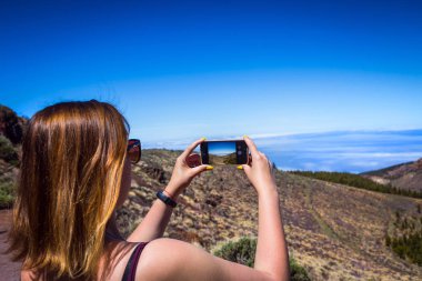 Tenerife, Kanarya Adaları, İspanya üzerinde fotoğrafta telefonunu şaşırtıcı dağlar peyzaj ile genç bir kadın. Seyahat kavramı