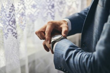 İş adamı kol saatini kontrol ediyor, saati eline alıyor, damat düğün töreninden önce hazırlanıyor.