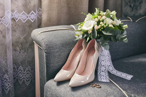 bridal accessories such as shoes, rings and bouquet  lie on a sofa