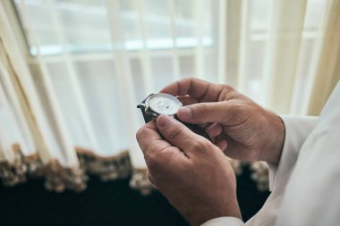 İş adamı kol saatini kontrol ediyor, saati eline alıyor, damat düğün töreninden önce hazırlanıyor.