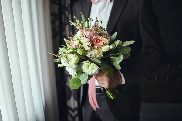 man holding bridal bouquet in hands, groom getting ready in the morning before wedding ceremony. Men Fashion