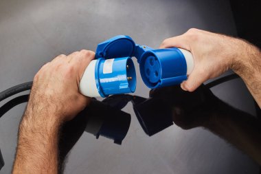 Elektrikli araba koyu arka plan üzerinde fiş şarj elini tutar. Çevre dostu alternatif enerji kavramı.