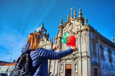 Young woman tourist with portuguese flag standing near the Congregados Carmelites church with famous portuguese blue tiles on the facade traveling in Porto city. Portugal clipart