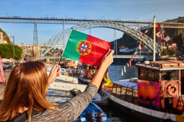 Portekiz bayrağı ile ayakta, Porto, Portekiz ışık sabah saatlerinde Douro nehir, köprü ve tekneler güzel cityscape manzarasının tadını genç kadın Gezgin 