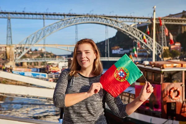 Ung kvinna traveler står tillbaka med portugisiska flaggan, njuter vackra stadsbilden syn på floden Douro, bridge och båtar under förmiddagen ljus i Porto, Portugal — Stockfoto