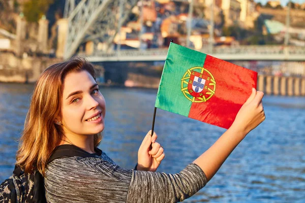 Young woman tourist with portuguese flag enjoying beautiful landscape view on the old town with river and famous iron bridge Dom Luiz during the sunset in Porto city, Portugal — Stock Photo, Image