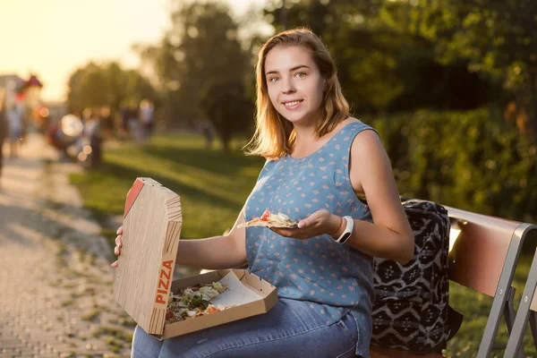 Feliz joven mujer sosteniendo pizza caliente en caja, asiento al aire libre en el parque — Foto de Stock