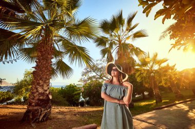Bodrum, Türkiye'de güneşli gün, tropikal palmiye ağaçları altında yürüyüş plaj şapka genç güzel kadın. Tatil açık havada deniz manzarası yaz seyahat kavramı 