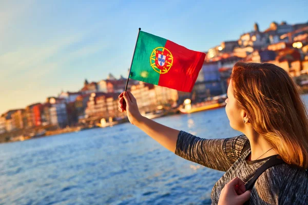 Joven turista con bandera portuguesa disfrutando de una hermosa vista del paisaje en el casco antiguo (barrio histórico de Ribeira) y el río Duoro durante la puesta de sol en la ciudad de Oporto, Portugal — Foto de Stock