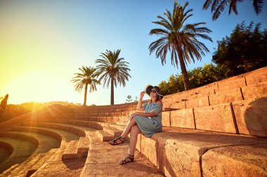 Bodrum, Türkiye'nin güneşli bir günde, bir antik amfitiyatro basamaklarında oturan plaj şapka genç güzel kadın. Tatil açık havada deniz manzarası yaz seyahat kavramı 