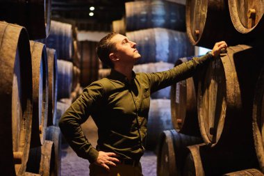 Italyan, Porto, Portekiz, Fransa 'da serin ve karanlık mahzende sıralı bir kasa içinde şarap ile eski yaşlı geleneksel ahşap varil profesyonel winemaker erkek