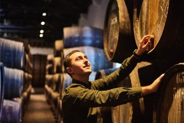 Italyan, Porto, Portekiz, Fransa 'da serin ve karanlık mahzende sıralı bir kasa içinde şarap ile eski yaşlı geleneksel ahşap varil profesyonel winemaker erkek