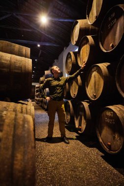 Italyan, Porto, Portekiz, Fransa 'da serin ve karanlık mahzende sıralı bir kasa içinde şarap ile eski yaşlı geleneksel ahşap varil profesyonel winemaker erkek