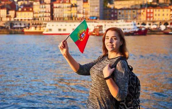 Joven turista con bandera portuguesa disfrutando de una hermosa vista del paisaje en el casco antiguo (barrio histórico de Ribeira) y el río Duoro durante la puesta de sol en la ciudad de Oporto, Portugal — Foto de Stock