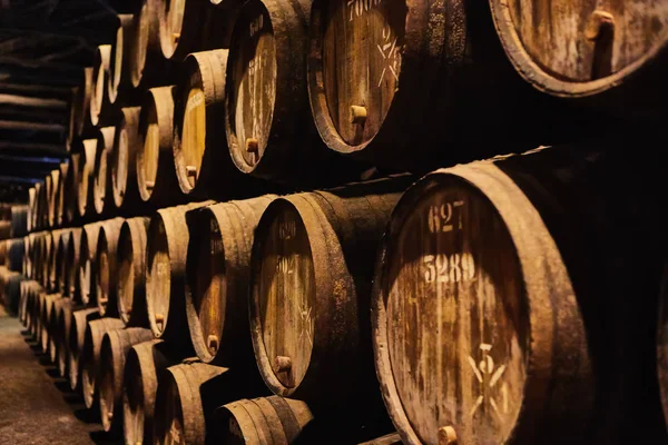 Viejos barriles de madera tradicionales envejecidos con vino en una bóveda alineada en una bodega fresca y oscura en Italia, Oporto, Portugal, Francia — Foto de Stock