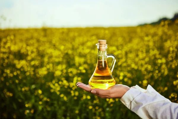 rapeseed oil bottle in hand of an agronomist or biologist on background rape field