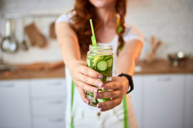 Genç kadın mutfakta camdan salatalık, limon ve nane yaprakları ile tatlı su içiyor. Sağlıklı Yaşam Tarzı ve Yeme. Sağlık, Güzellik, Diyet Kavramı.