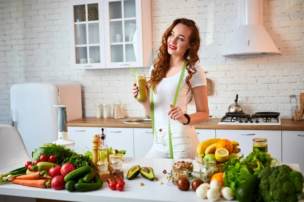 과일과 야채와 부엌 테이블에 녹색 스무디를 마시는 젊은 여성. 건강한 식생활 개념. 비건 식사 및 해독 메뉴 — 스톡 사진