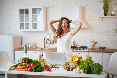 Modern mutfakta yemek yaparken bir dizüstü bilgisayar kullanarak genç güzel kadın. Sağlıklı gıda ve Diyet kavramı. Kilo Verme