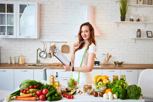 Young beautiful woman using tablet with infographic while cooking in the modern kitchen. Healthy eating, vitamins, dieting, technology and people concept. Losing Weight