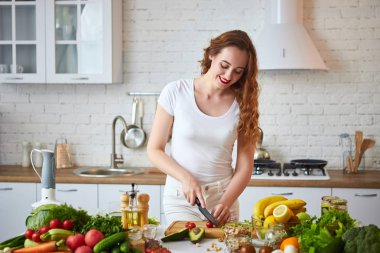 Genç mutlu kadın Yeşil taze malzemelerle kapalı güzel mutfakta salata yapmak için domates kesme. Sağlıklı gıda ve diyet konsepti. Kilo kaybetme