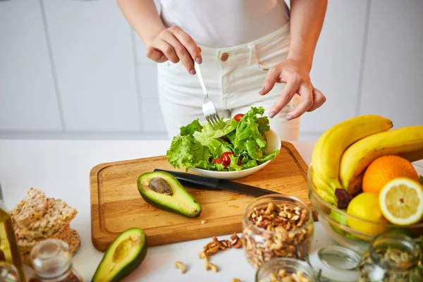 Νέα χαρούμενη γυναίκα προετοιμάζει νόστιμη σαλάτα στην όμορφη κουζίνα με πράσινα φρέσκα υλικά σε εσωτερικούς χώρους. Υγιεινά φαγητά και δίαιτες. Χάνοντας βάρος — Φωτογραφία Αρχείου