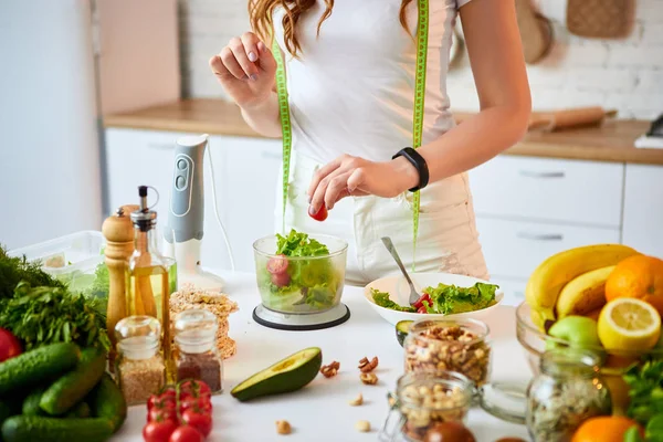 Νέα χαρούμενη γυναίκα προετοιμάζει νόστιμη σαλάτα στην όμορφη κουζίνα με πράσινα φρέσκα υλικά σε εσωτερικούς χώρους. Υγιεινά φαγητά και δίαιτες. Χάνοντας βάρος — Φωτογραφία Αρχείου