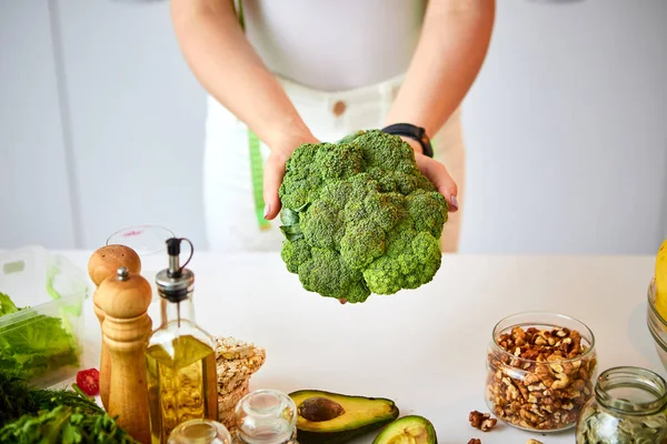 Νέα ευτυχισμένη γυναίκα κρατώντας μπρόκολο στην όμορφη κουζίνα με πράσινα φρέσκα υλικά σε εσωτερικούς χώρους. Υγιεινά φαγητά και δίαιτες. Χάνοντας βάρος — Φωτογραφία Αρχείου