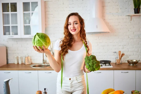 Jovem mulher feliz segurando brócolis e repolho na bela cozinha com ingredientes frescos verdes dentro de casa. Alimentação saudável e conceito de dieta. Perder peso — Fotografia de Stock