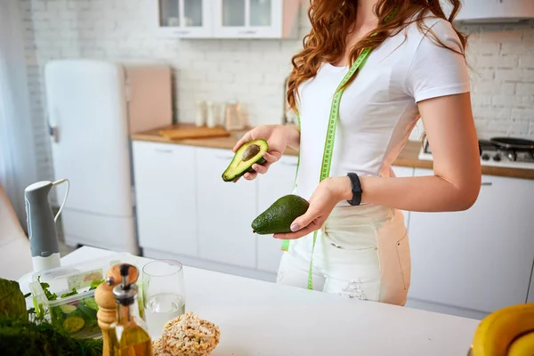 실내에서 녹색 신선한 재료와 아름다운 부엌에서 샐러드를 만들기위한 아보카도를 들고 젊은 행복한 여성. 건강한 음식과 다이어트 개념. 체중 감량 — 스톡 사진