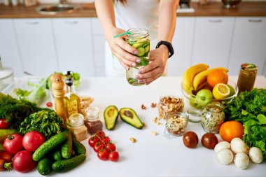 Genç kadın mutfakta camdan salatalık, limon ve nane yaprakları ile tatlı su içiyor. Sağlıklı Yaşam Tarzı ve Yeme. Sağlık, Güzellik, Diyet Kavramı.