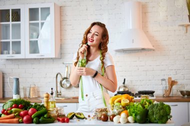 Genç kadın camdan tatlı su içiyor ve mutfakta başparmaklarını gösteriyor. Sağlıklı Yaşam Tarzı ve Yeme. Sağlık, Güzellik, Diyet Kavramı.