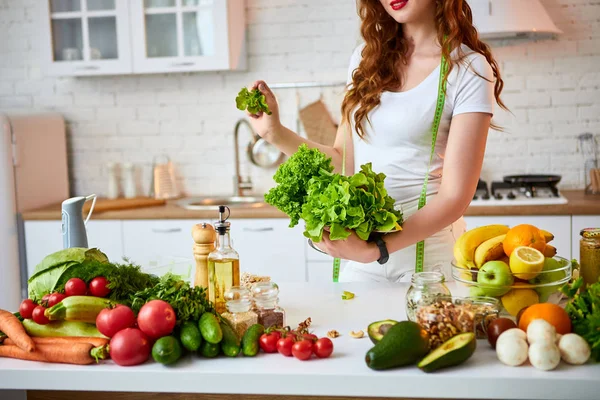 Νέα ευτυχισμένη γυναίκα κρατώντας φύλλα μαρούλι για την κατασκευή σαλάτα στην όμορφη κουζίνα με πράσινα φρέσκα υλικά σε εσωτερικούς χώρους. Υγιεινά φαγητά και δίαιτες. Χάνοντας βάρος — Φωτογραφία Αρχείου