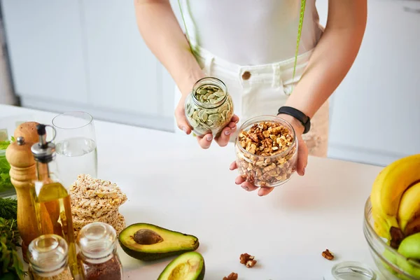 Νεαρή ευτυχισμένη γυναίκα που τρώει διαφορετικά καρύδια (κάσιους, φουντούκι, αμύγδαλο) στη σύγχρονη κουζίνα. Υγιεινά φαγητά και δίαιτες. Χάνοντας βάρος — Φωτογραφία Αρχείου