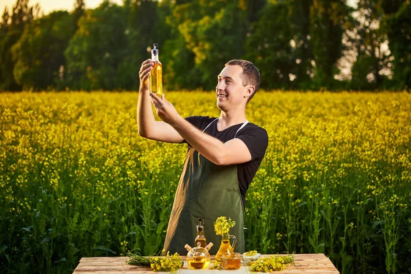 Un joven agricultor o agrónomo examina la calidad del aceite de colza en un campo de violación. Concepto agronegocio — Foto de Stock