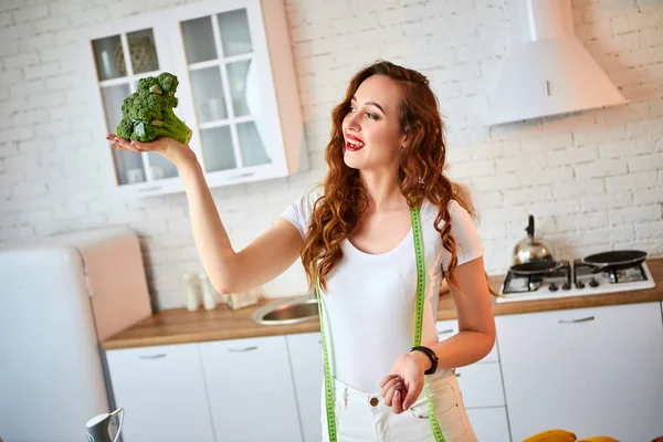 Jovem mulher feliz segurando brócolis na bela cozinha com ingredientes frescos verdes dentro de casa. Alimentação saudável e conceito de dieta. Perder peso — Fotografia de Stock