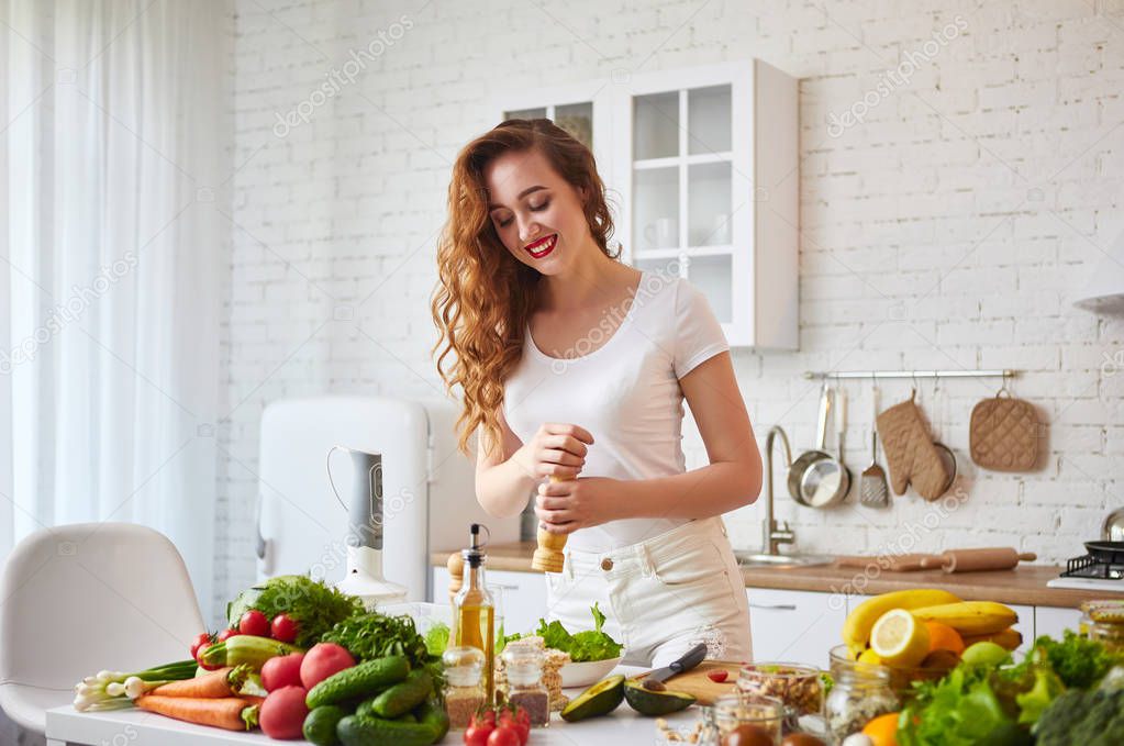 Young happy woman preparing tasty salad in the beautiful kitchen with green fresh ingredients indoors. Healthy food and Dieting concept. Loosing Weight