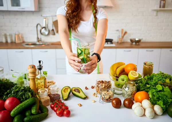 Νεαρή γυναίκα που πίνει φρέσκο νερό με αγγούρι, λεμόνι και φύλλα μέντας από γυαλί στην κουζίνα. Υγιής τρόπος ζωής και φαγητό. Υγεία, ομορφιά, δίαιτα ιδέα. — Φωτογραφία Αρχείου