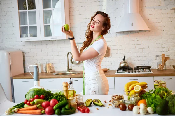 Fiatal boldog nő eszik almát a gyönyörű konyhában, zöld friss alapanyagokból beltérben. Egészséges táplálkozás és a fogyókúra fogalmát. Elvesztése súly — Stock Fotó