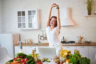 Modern mutfakta yemek yaparken bir dizüstü bilgisayar kullanarak genç güzel kadın. Sağlıklı gıda ve Diyet kavramı. Kilo Verme