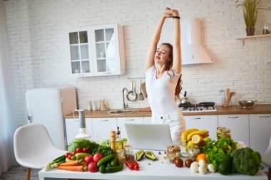 Modern mutfakta yemek yaparken bir dizüstü bilgisayar kullanarak genç güzel kadın. Sağlıklı gıda ve Diyet kavramı. Kilo Verme