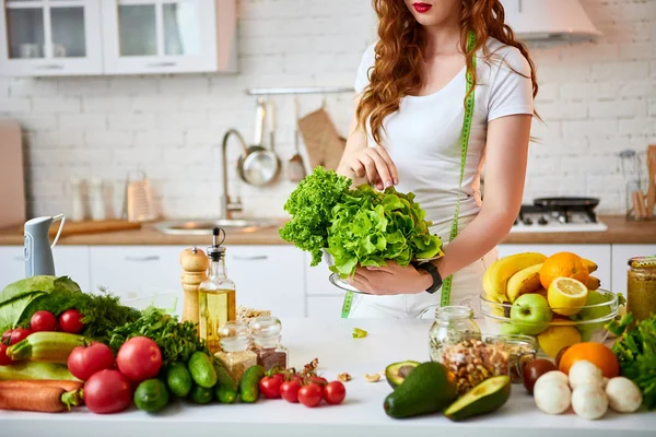 Νέα ευτυχισμένη γυναίκα κρατώντας φύλλα μαρούλι για την κατασκευή σαλάτα στην όμορφη κουζίνα με πράσινα φρέσκα υλικά σε εσωτερικούς χώρους. Υγιεινά φαγητά και δίαιτες. Χάνοντας βάρος — Φωτογραφία Αρχείου